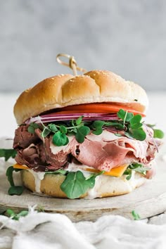 a sandwich with meat, cheese and vegetables on a wooden board next to a white cloth