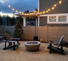 a fire pit sitting in the middle of a yard next to two chairs and a table