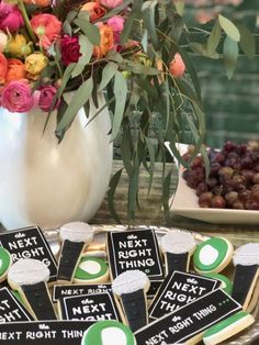 decorated cookies on a tray with flowers in the vase and next to it is a bowl of grapes