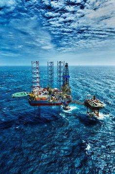 an oil rig in the middle of the ocean under a cloudy blue sky with clouds