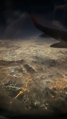 an aerial view of the city lights and clouds at night from inside an airplane window