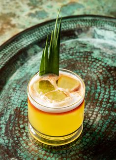 a drink with a green garnish sits on a glass plate