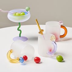 three different colored glass cups sitting on top of a white table next to each other