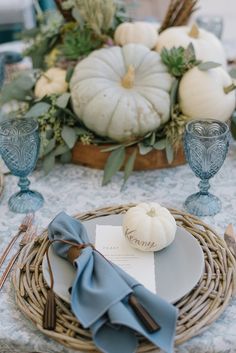 a place setting with blue napkins and white pumpkins