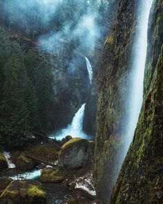 a waterfall in the middle of a forest with moss growing on it's sides