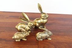 two brass rabbits sitting on top of a wooden table next to each other with their tails curled up