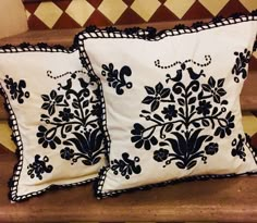 two black and white pillows sitting on top of a wooden bench next to each other