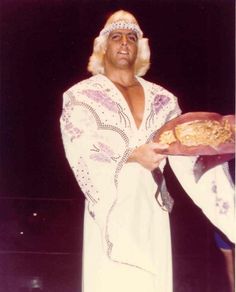 a man dressed in white holding a plate with food on it and wearing a headdress