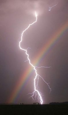 a rainbow appears to be in the middle of a dark sky with two lightnings