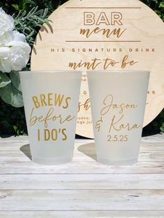 two shot glasses sitting next to each other on top of a wooden table with flowers in the background