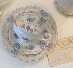 an antique china tea cup and saucer with blue flowers on it, next to a note