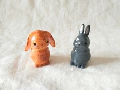 two small ceramic animals sitting next to each other on a white cloth covered tablecloth