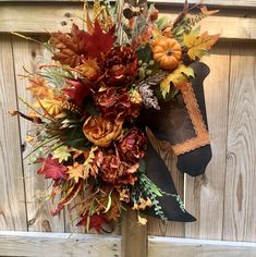 a fall wreath with leaves and flowers hanging on a wooden fence