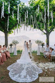 a bride and groom standing under an arbor with flowers on the ground in front of them