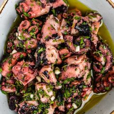 an octopus dish is served in a white bowl with green garnish on top