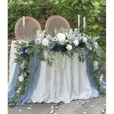 the table is decorated with blue and white flowers, greenery and candles for an elegant touch