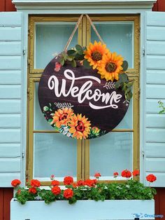 a welcome sign hanging on the side of a window sill with flowers in it