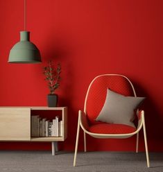 a red room with a chair, book shelf and lamp on the side table next to it