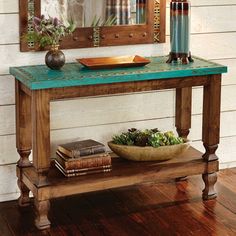 a wooden table topped with a bowl of flowers next to a mirror and candle holder