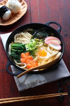 a bowl of ramen with vegetables and noodles on a wooden table next to chopsticks