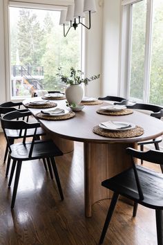 a dining room table set with place settings and plates on it, in front of large windows