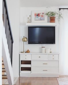 a flat screen tv sitting on top of a white dresser next to a stair case