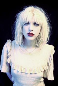 a woman with blonde hair and blue eyes posing for a photo in front of a black background