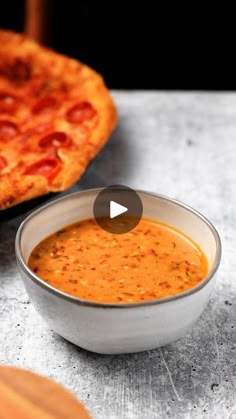 a bowl of tomato soup next to a pizza