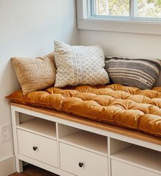 a bench with pillows on it in front of a window