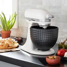 a white mixer sitting on top of a kitchen counter next to some vegetables and bread