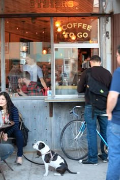 people sitting at tables in front of a coffee shop with a dog on the leash