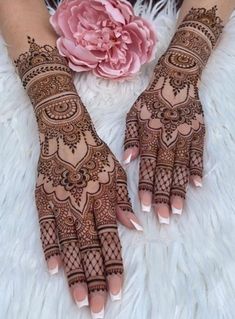 two hands with henna designs on them and a pink flower in the middle of each hand