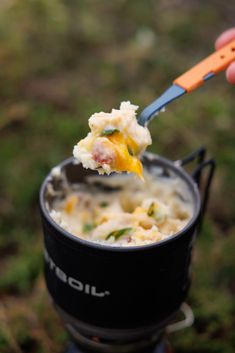 a person holding a spoon full of food in a black cup with an orange handle