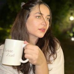 a woman holding a white coffee mug in her right hand and looking off to the side