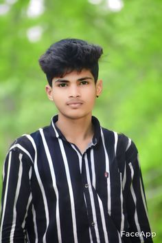 a young man with black and white striped shirt posing for a photo in front of trees