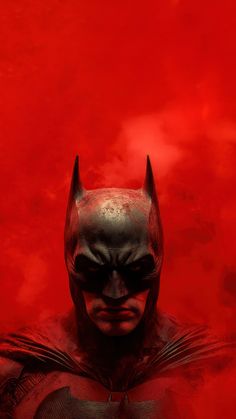 a man dressed as batman standing in front of a red background with clouds and fog