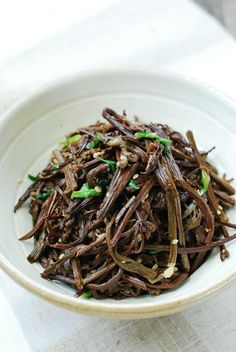 a white bowl filled with brown and green stir fried food on top of a table