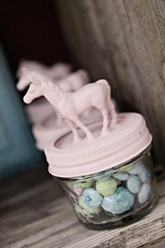 small plastic horses in a glass jar on a wooden shelf next to rocks and candy