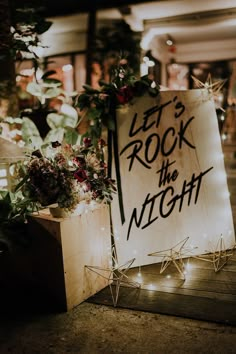 a sign that says let's rock the night next to some flowers and plants