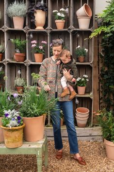 a woman holding a child in front of potted plants