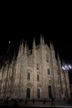 the cathedral is lit up at night with people walking in front and onlookers