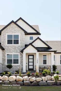 a large white house with black trim and stone wall around the front door is shown