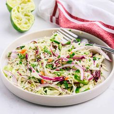 a white bowl filled with coleslaw salad next to two limes and a fork