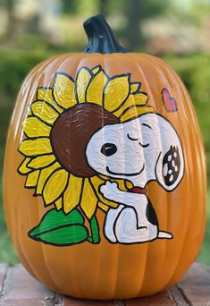 a pumpkin decorated with a snoopy dog and sunflower on the front, sitting on a brick surface