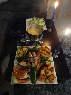 a table with food and candles on it in front of a couch next to a lit candle