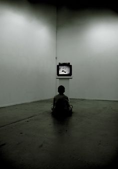 a person sitting on the floor in front of a flat screen tv, watching it