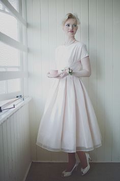 a woman in a white dress standing next to a window