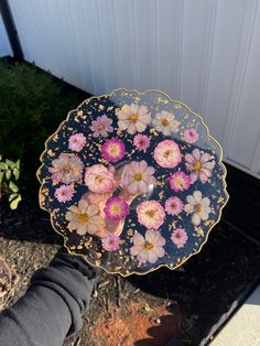 a hand holding a plate with flowers painted on the side and gold trim around it