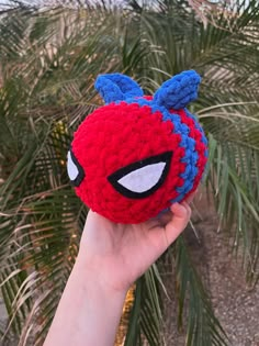 someone is holding up a crocheted spider - man mask in front of some palm trees