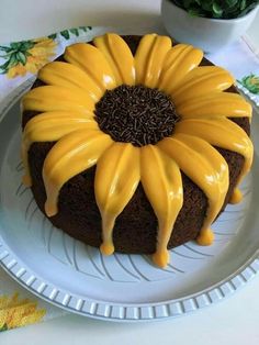 a cake with yellow icing sitting on a plate next to a potted plant